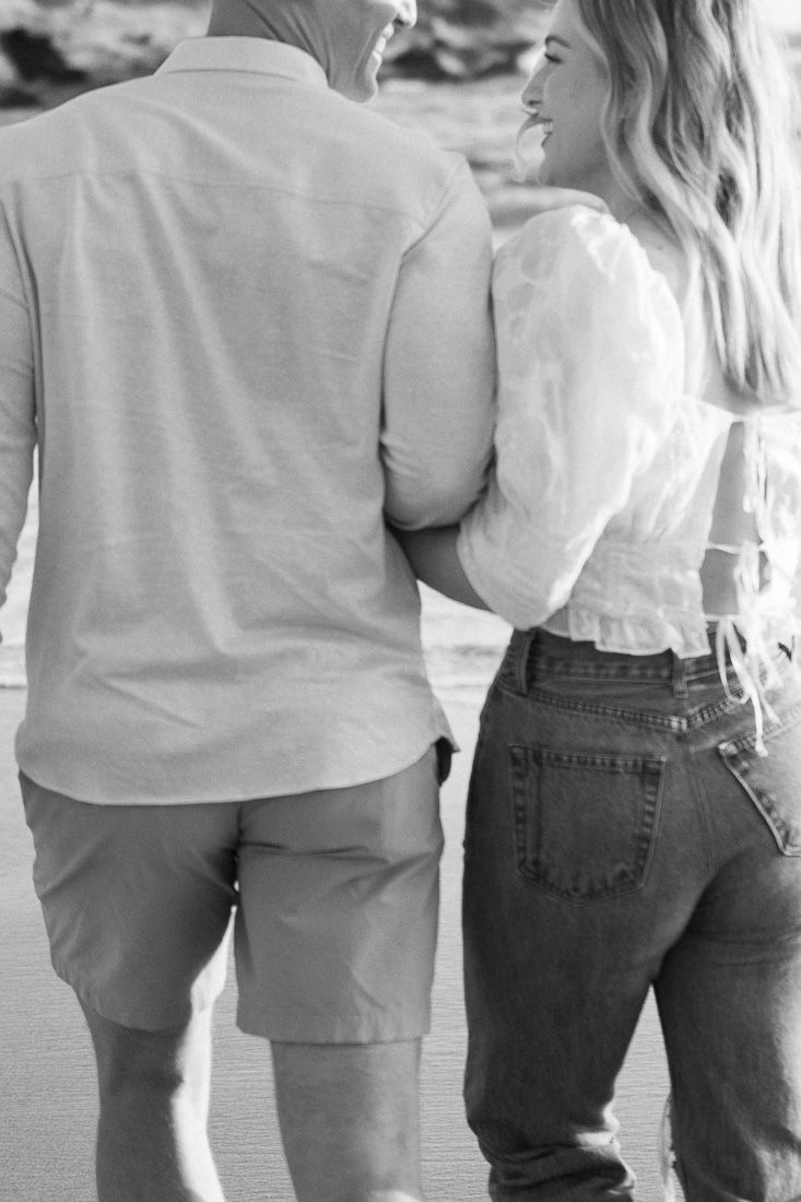 Black and white photo of a couple standing close together on the beach.
