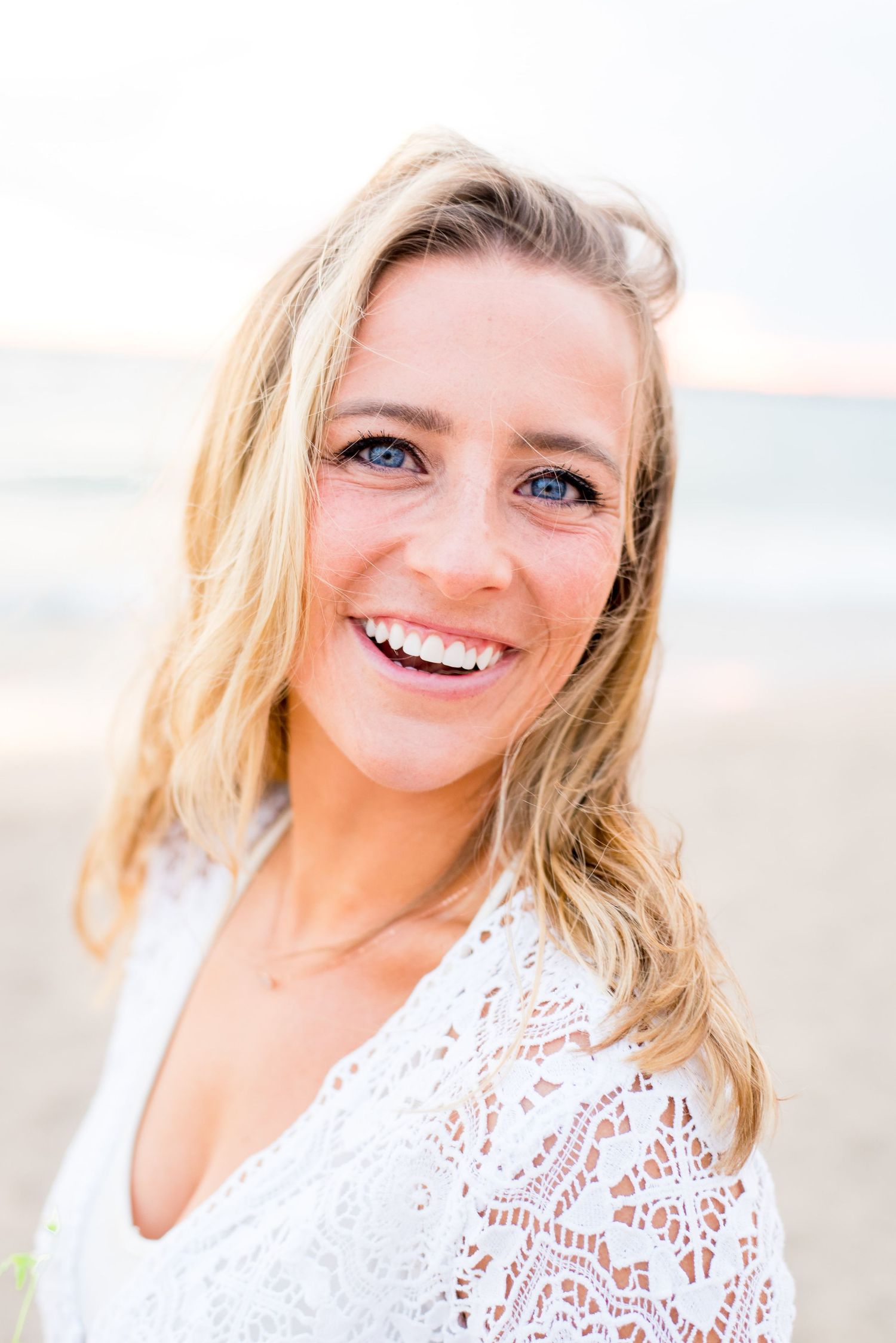 blonde woman in white lace dress smiles on North Avenue Beach Chicago during sunrise