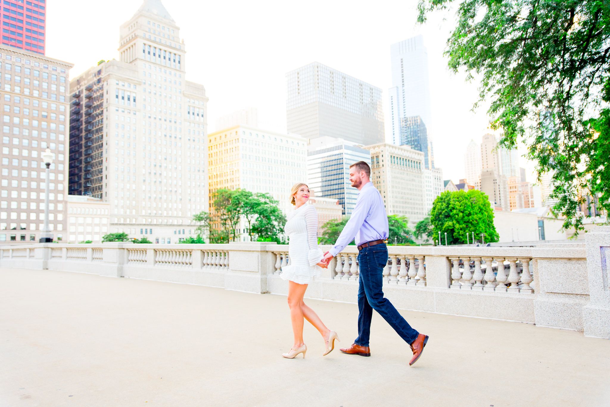woman in short white dress leading man in jeans across bridge with Chicago skyline in background