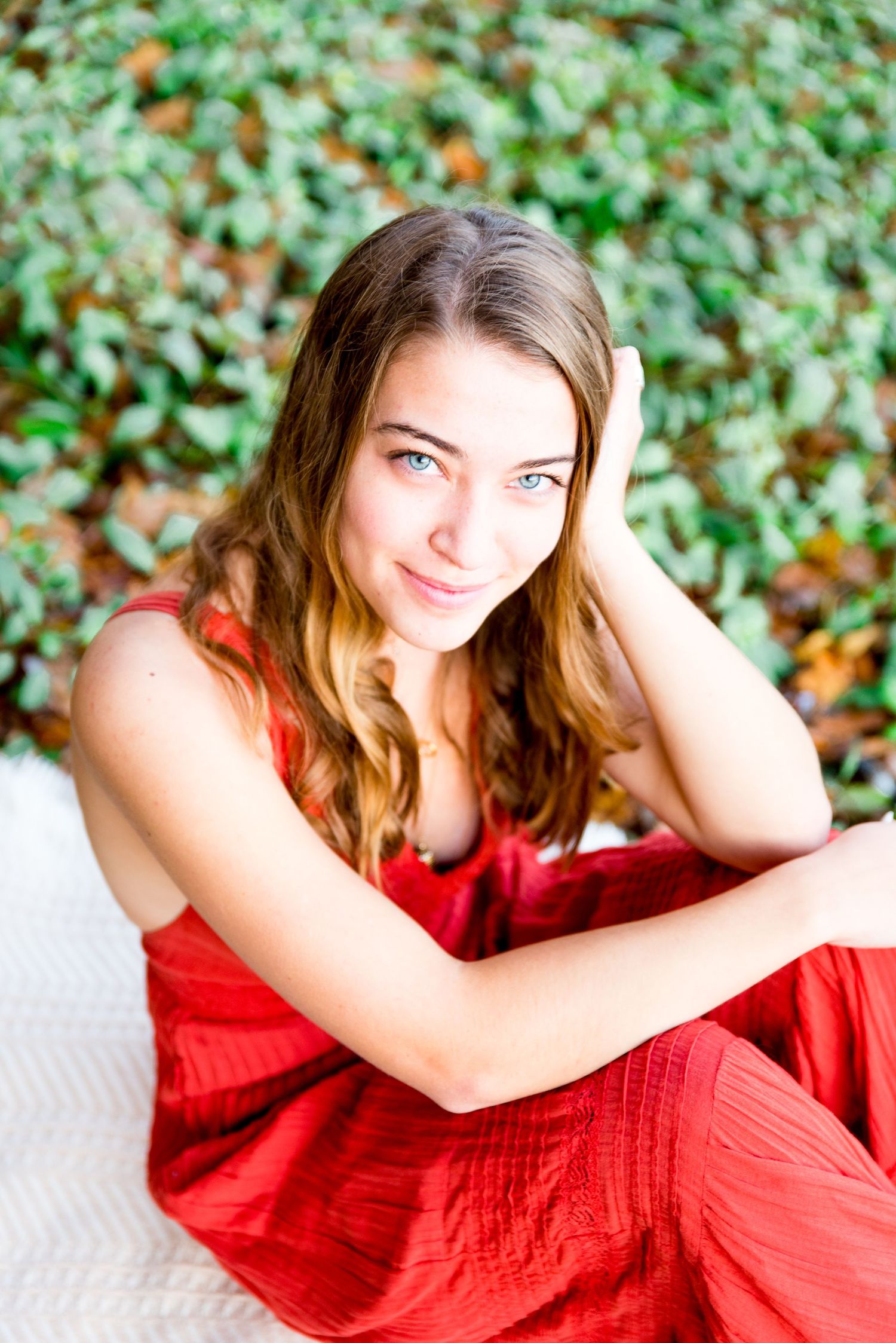young woman with blue eyes sitting and putting hand on head, softly smiling for senior pictures in Chicago