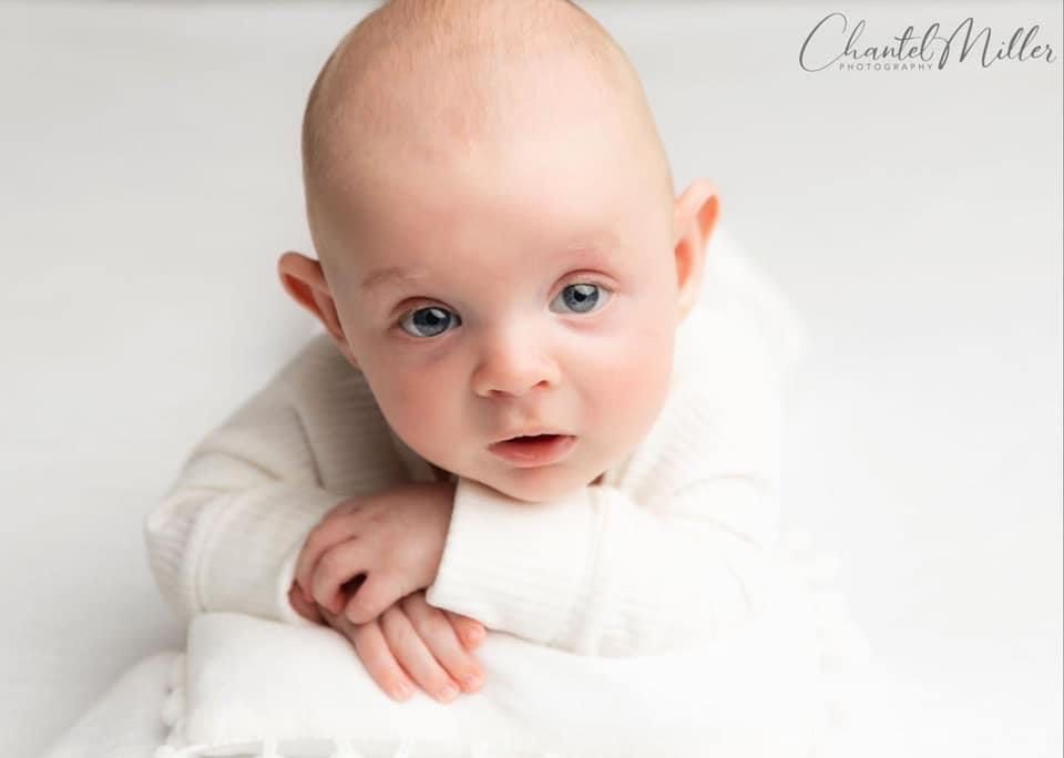 baby boy dressed in white with chin on hands