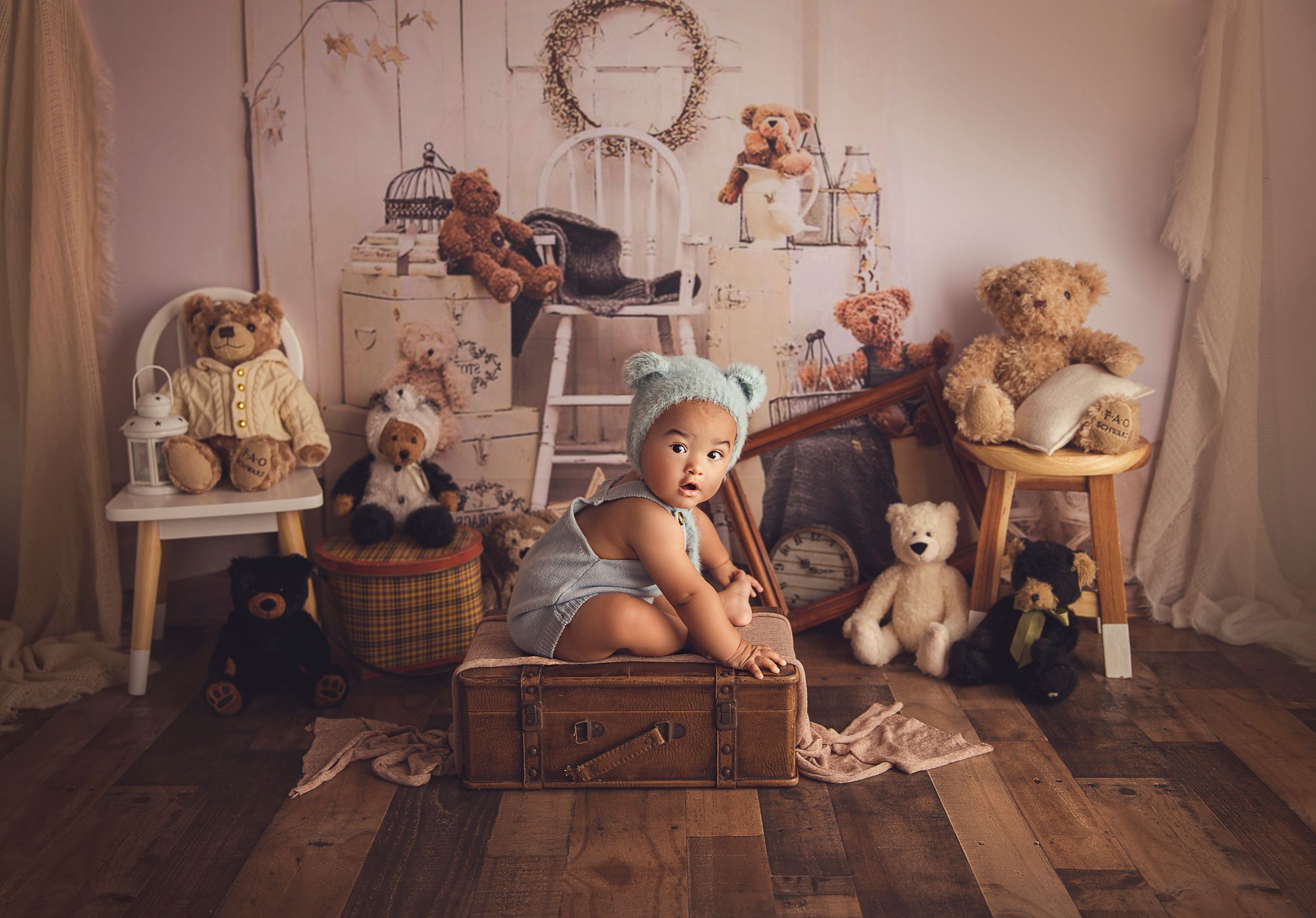 7 months old baby boy sitting on suitcase with blue bear bonnet