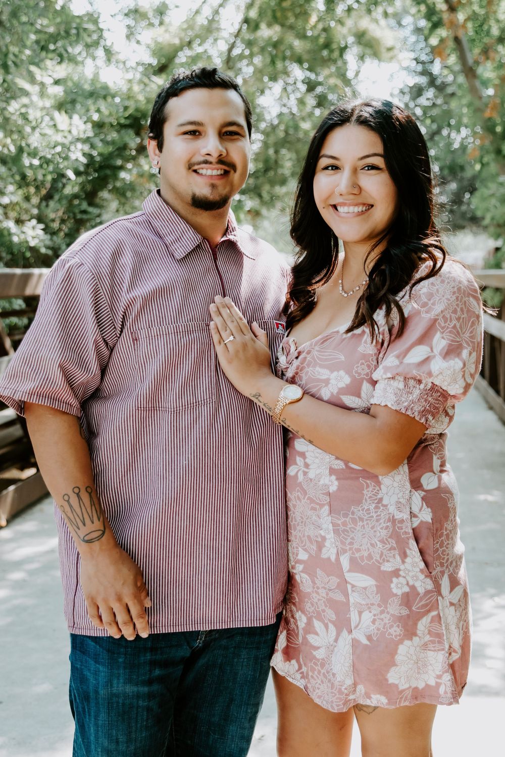 Newly engaged couple posing together on wooden bridge in casual attire.