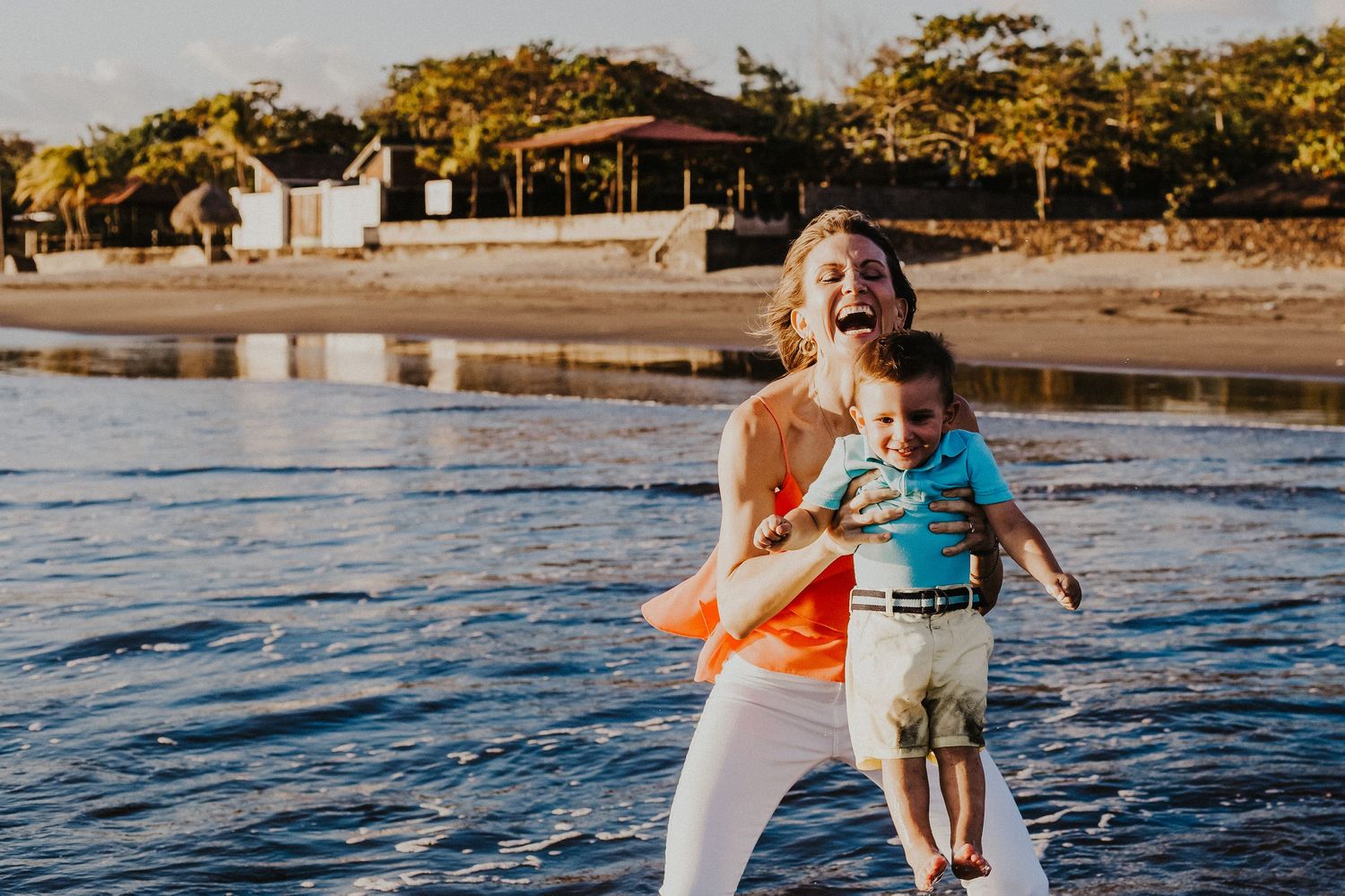 mother lifts son into the air over the water on the beach while laughing
