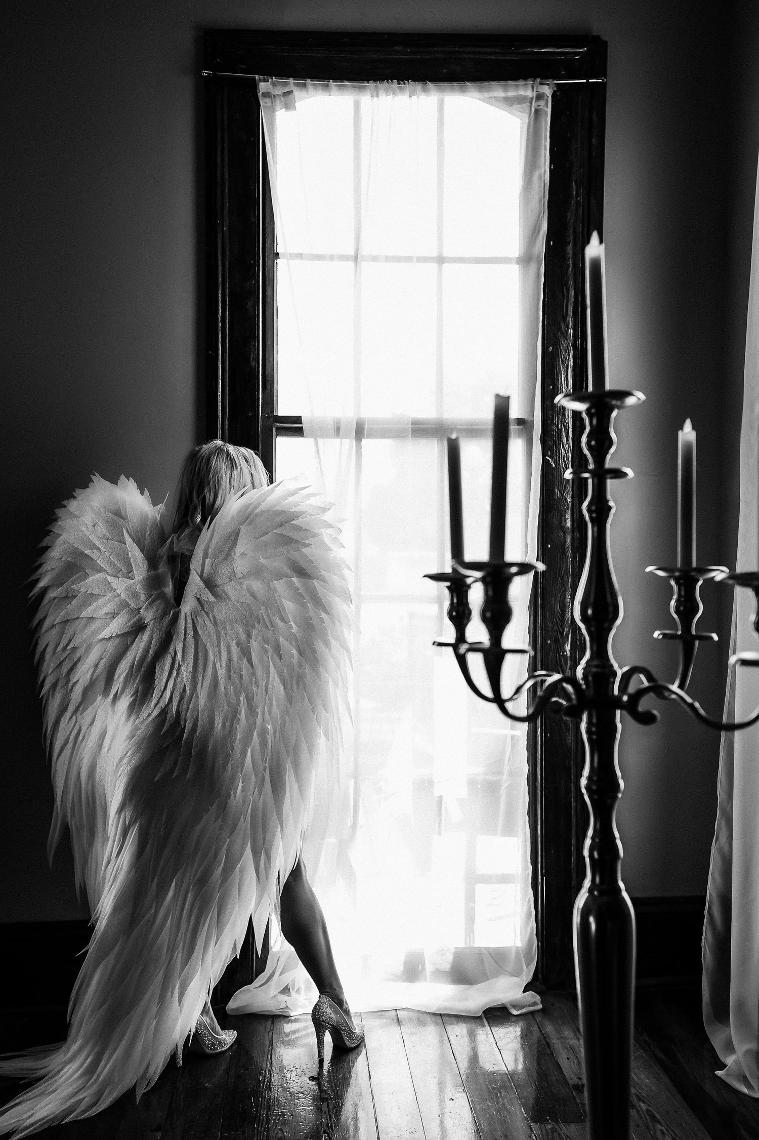Dramatic black and white photo of angel wings and candelabra by window.