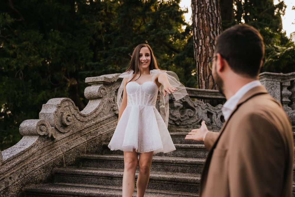 A bride in a short white dress poses on historic stone steps during a wedding photoshoot.