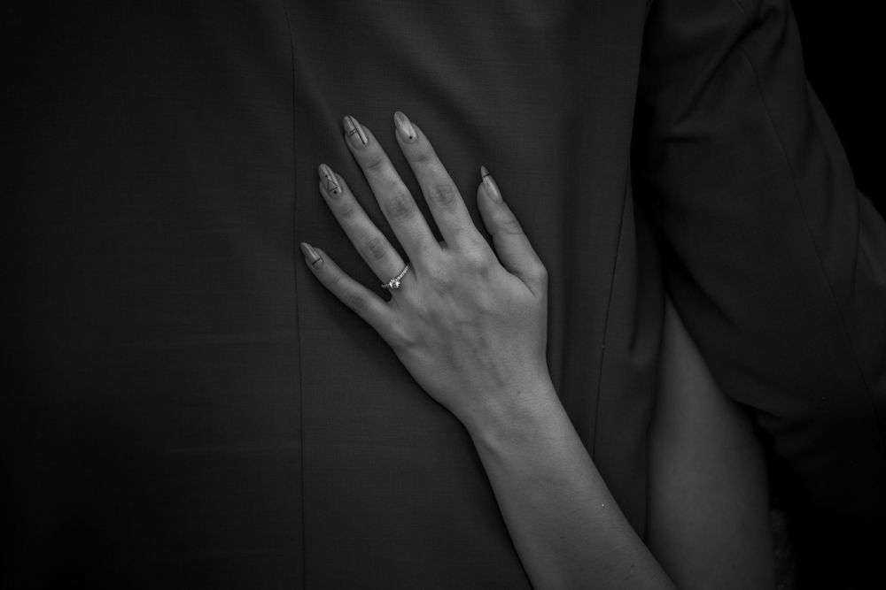 Close-up of hands tenderly placed against formal black attire in intimate moment.