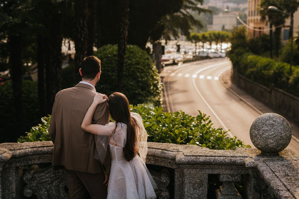 A couple stands on a stone balcony overlooking a winding road during a romantic photoshoot.