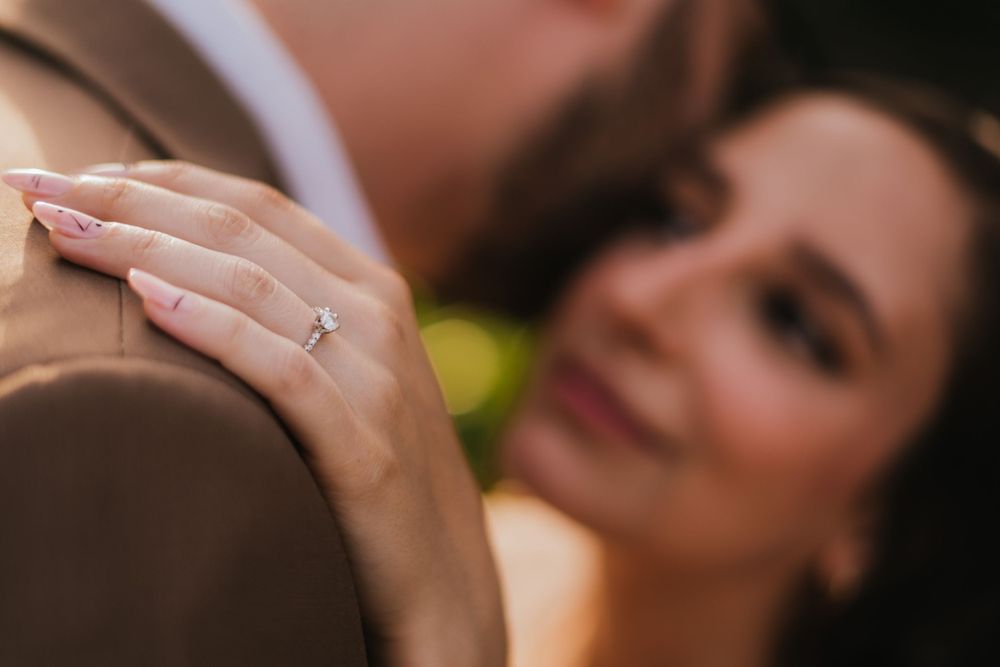 Close-up shot of an engagement ring as a couple embraces during their photoshoot.