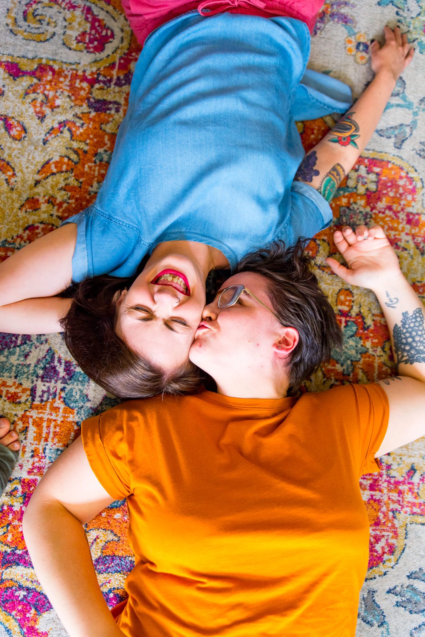 two woman laying on pink orange and blue rug, kissing one on forehead for chicago couples pictures