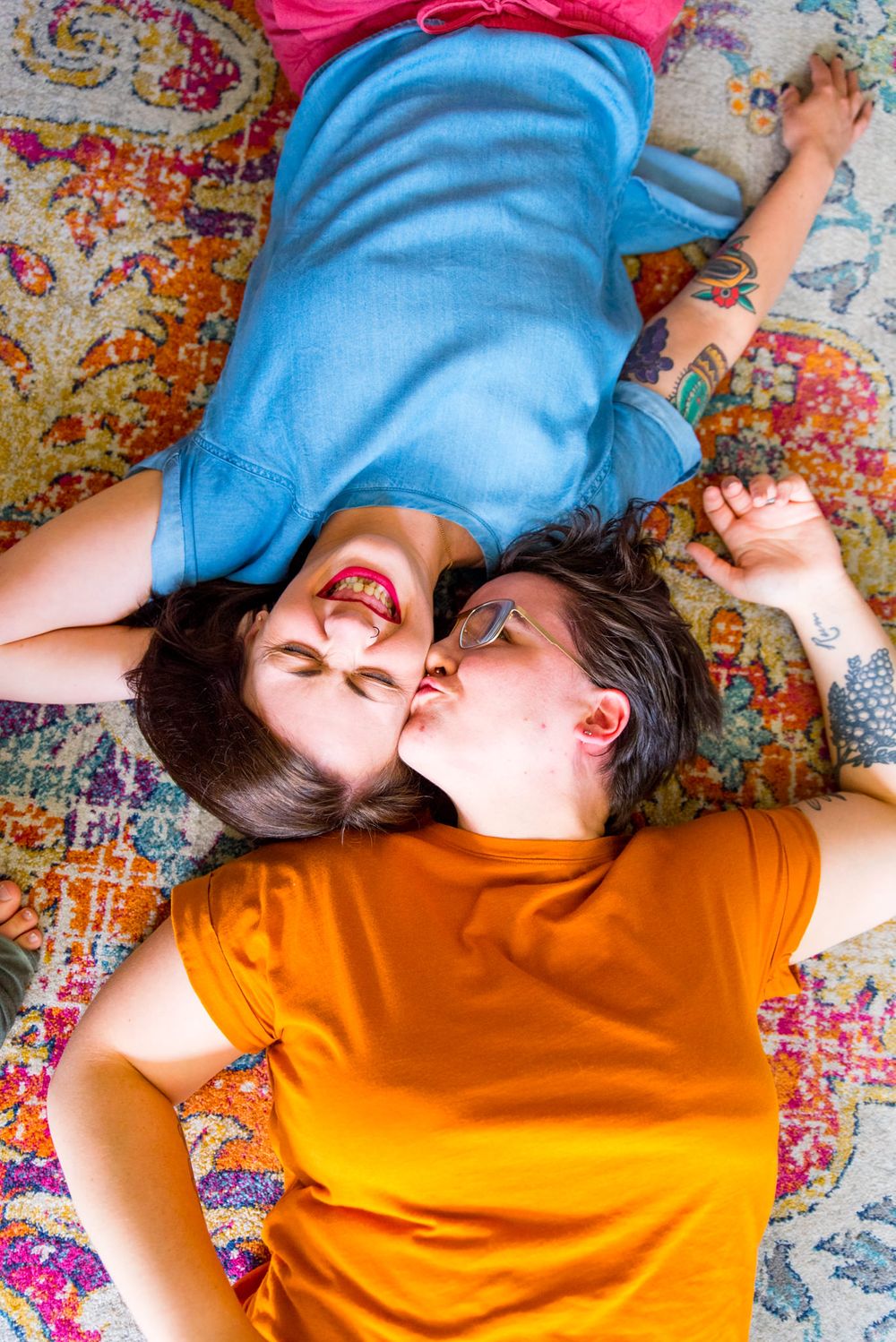 two woman laying on pink orange and blue rug, kissing one on forehead for chicago couples pictures