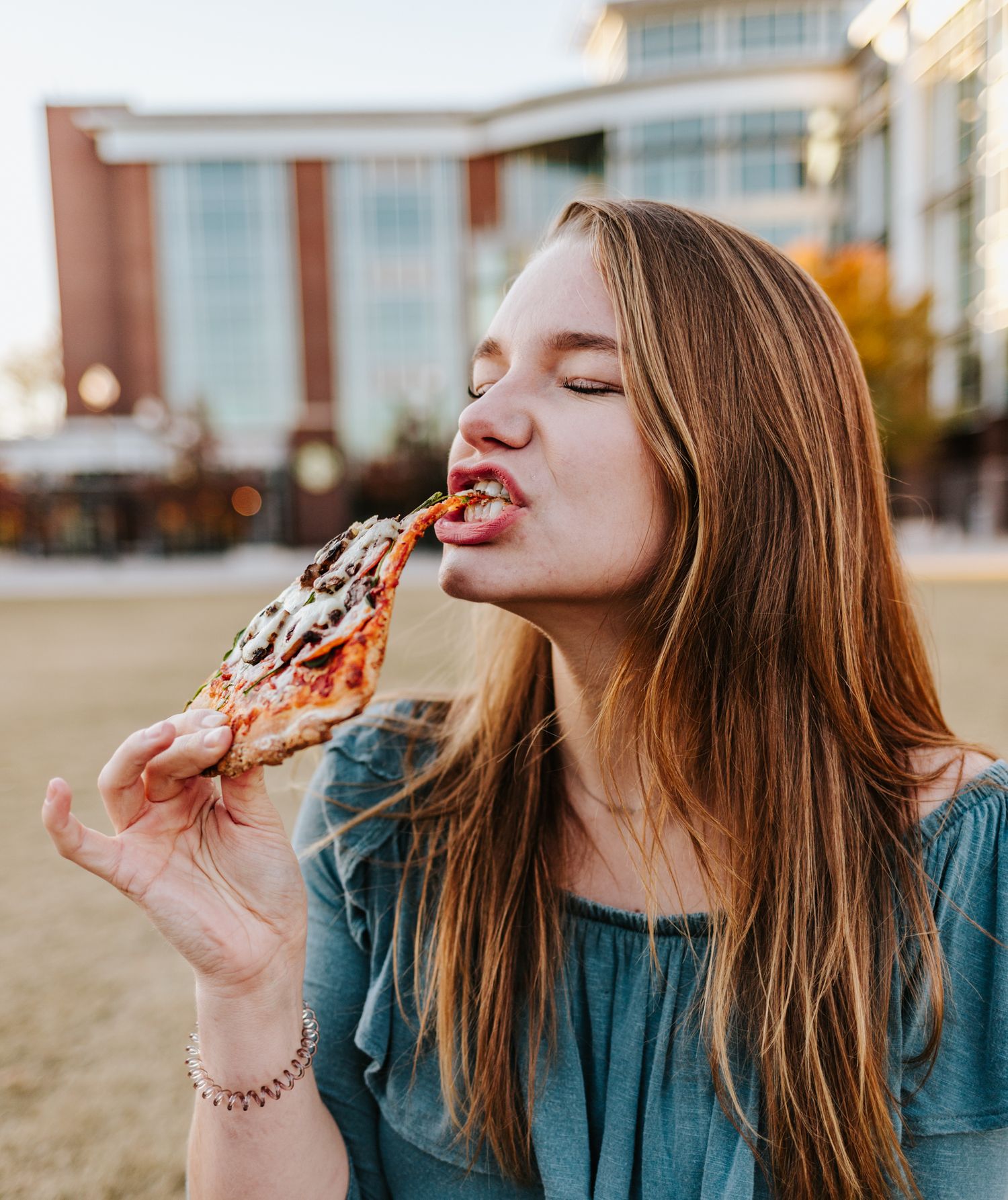College student eating pizza in front of her college for her senior portraits.