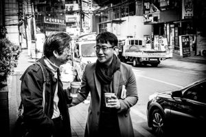 Black and white photo of two men sharing coffee in street of Soul South Korea