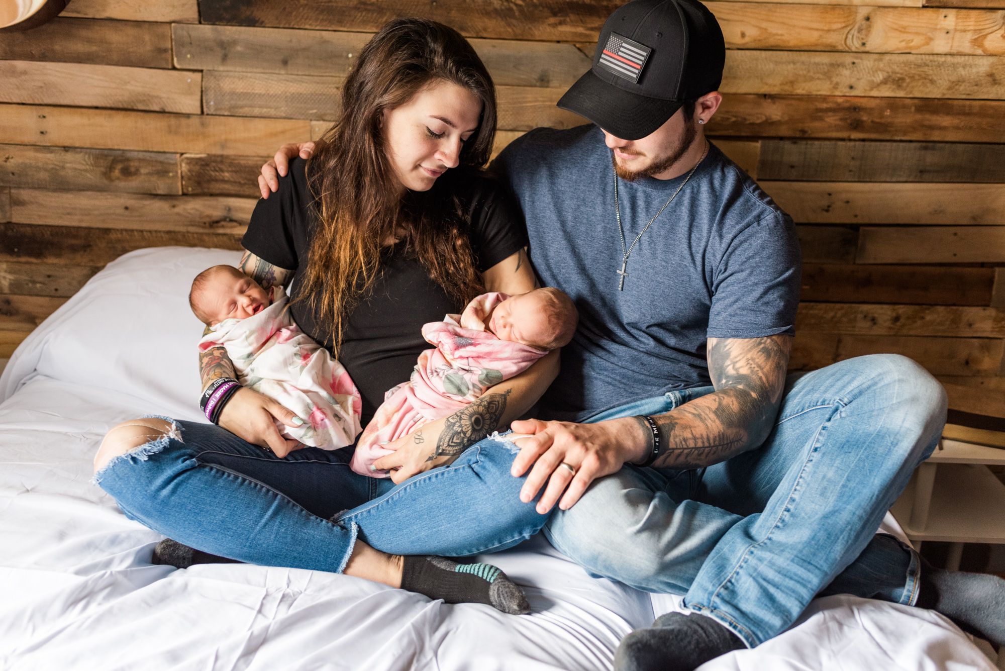 Mom and dad holding newborn twin girls on bed in rustic home in Corsica,
