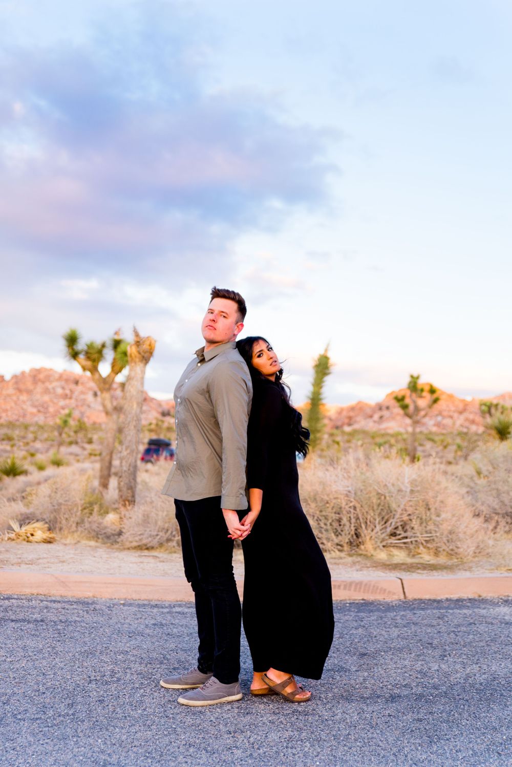 man in gray shirt and woman in black dress stand back to back under the blue sky at Joshua Tree National Park