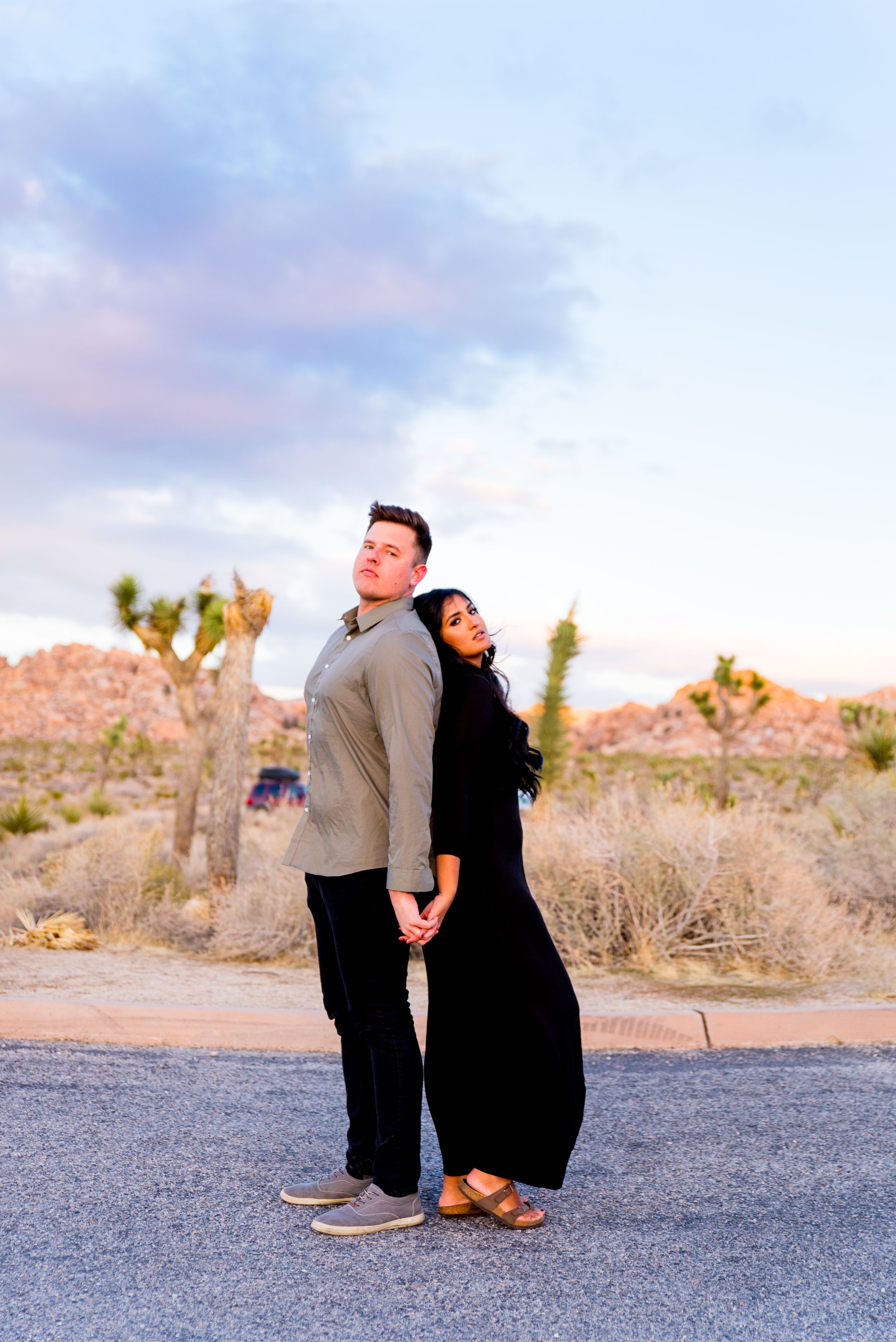 man in gray shirt and woman in black dress stand back to back under the blue sky at Joshua Tree National Park