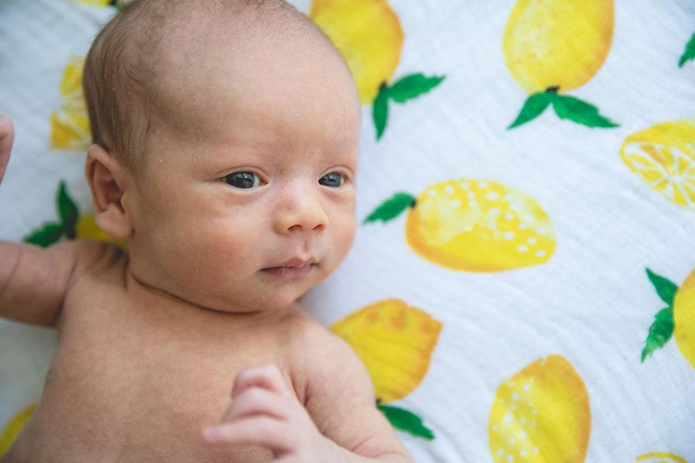 newborn baby boy laying on a lemon print blanket with eyes open