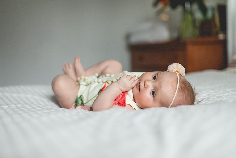 6 month old baby girl laying on a bed with her legs curled in like a frog and smiling