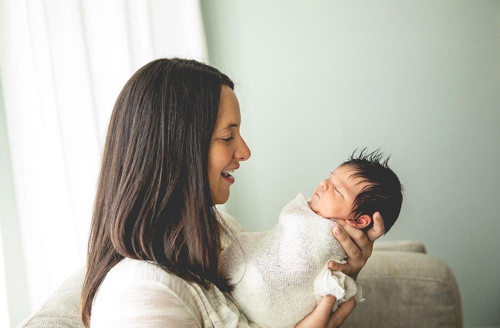 mother holds newborn girl in front of her and looks at her baby