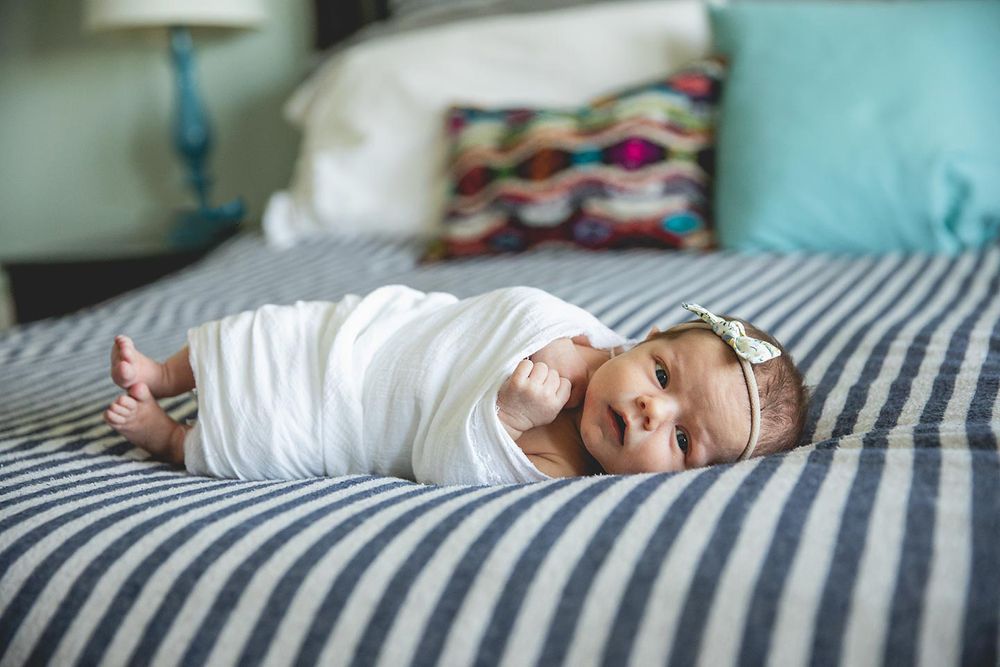 newborn baby girl laying on bed as she is swaddled in a white swaddle