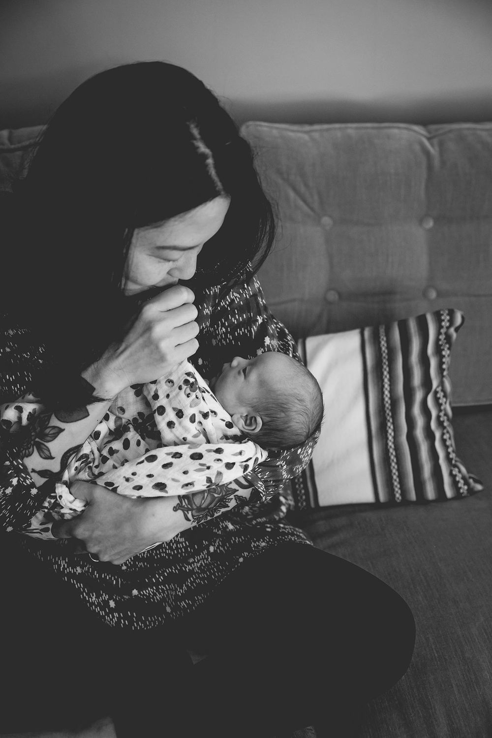 mother kissing her newborn baby boy on his tiny hand while she sits on the couch