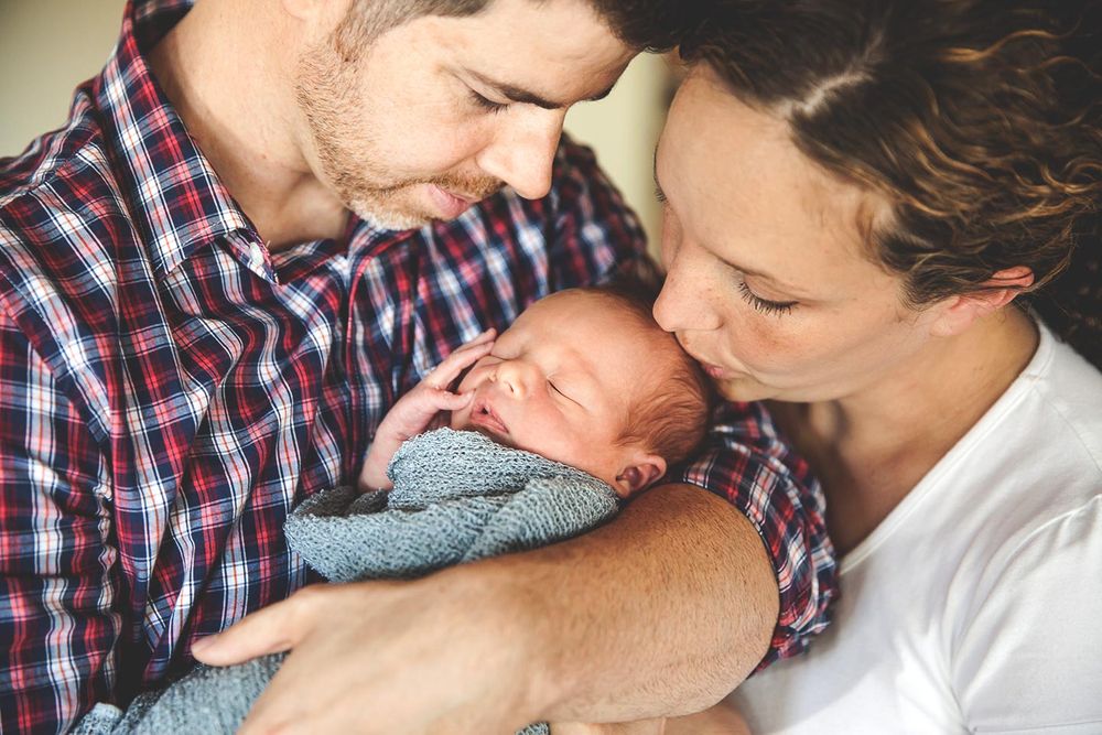 father holds newborn baby son while mother hugs him and kisses her baby