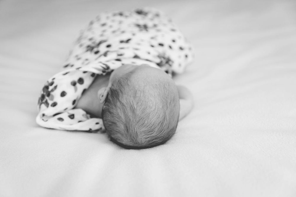 newborn boy lays on bed in a loosely wrapped blanket