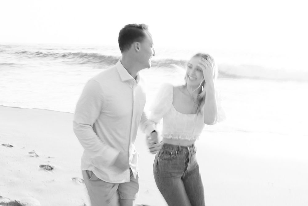 Black and white photo of a couple laughing together on a sunny beach.