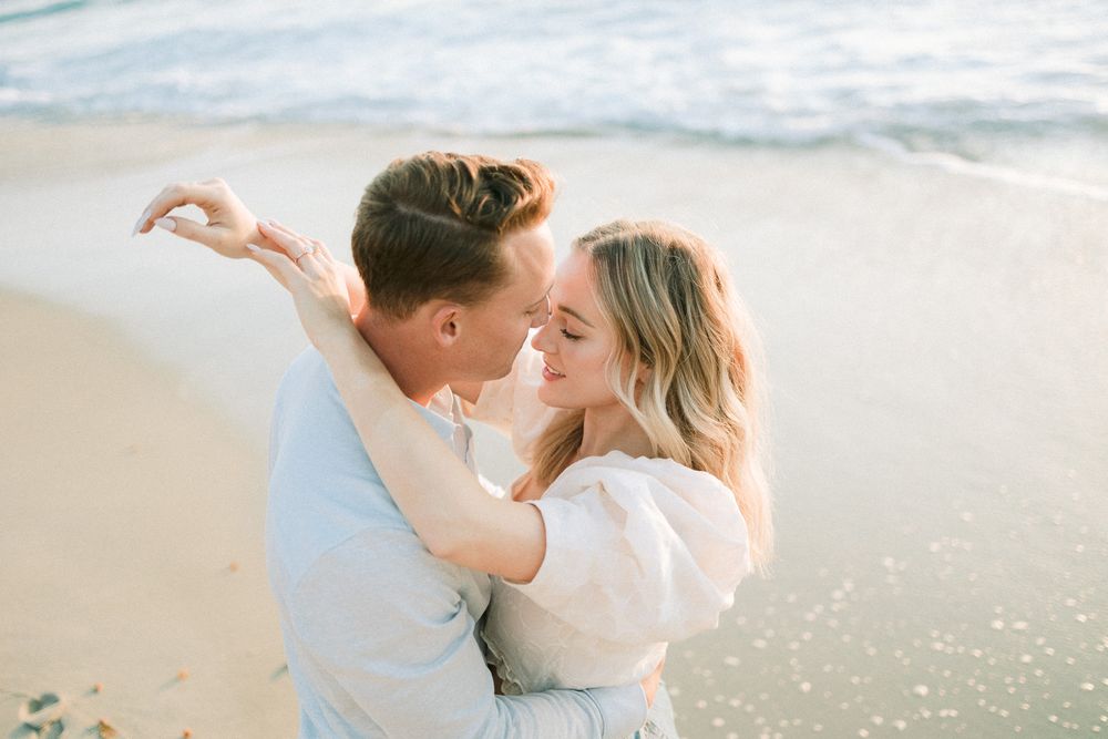 A romantic embrace on the beach with soft sunlight and ocean waves in the background.