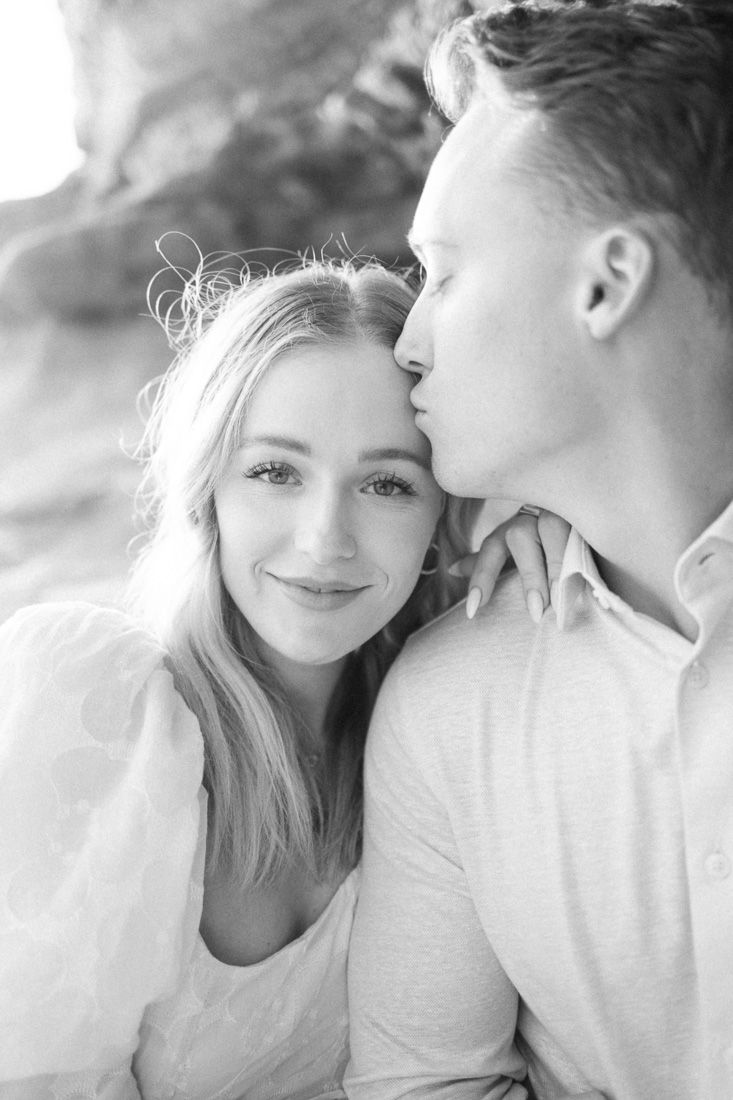 An intimate black and white portrait of a couple sharing a close moment by the ocean.