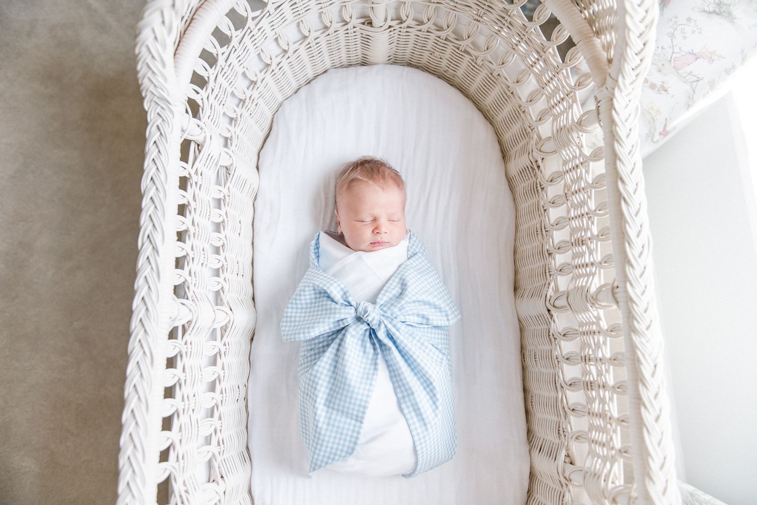Newborn baby boy asleep in his white bassinet swaddled in a Beaufort Bonnet bow sash