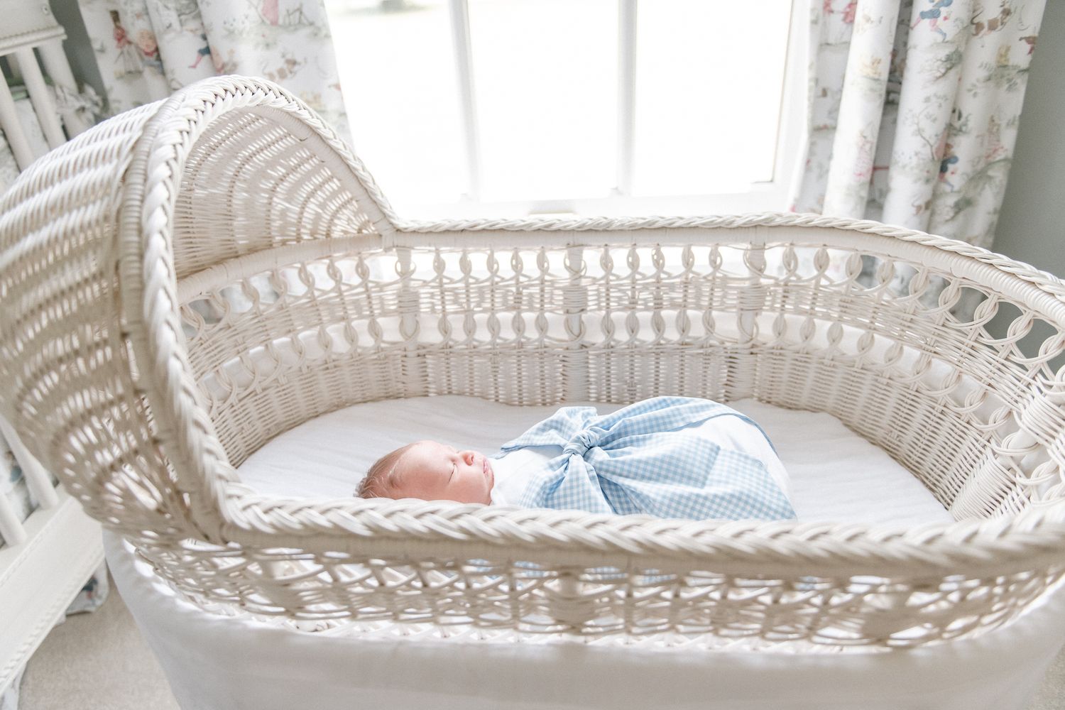Newborn baby sleeps in his Pottery Barn Kids bassinet swaddled in a Beaufort Bonnet bow sash