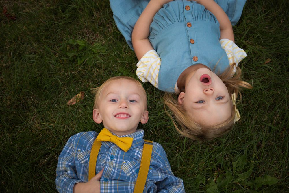 brother and sister laying in grass looking up at camera