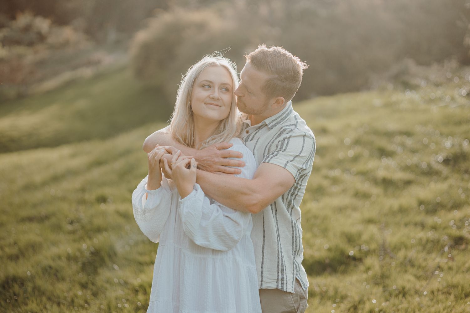 Tender embrace captured during golden hour in a scenic meadow setting.