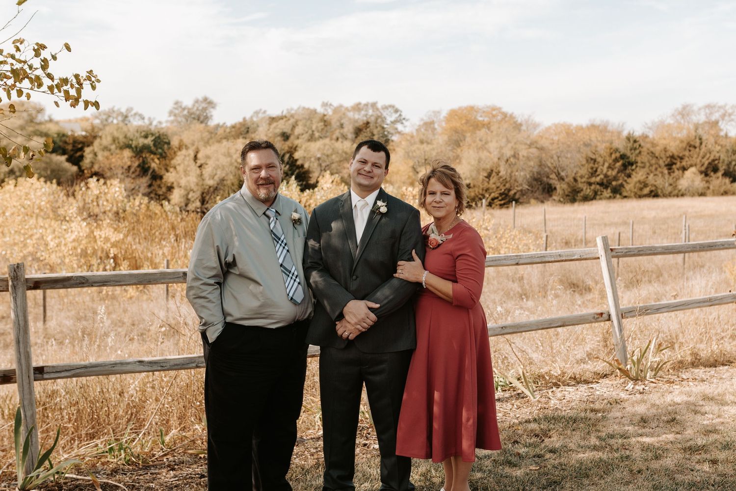 Family portrait outdoors with couple and parents against wooden fence.