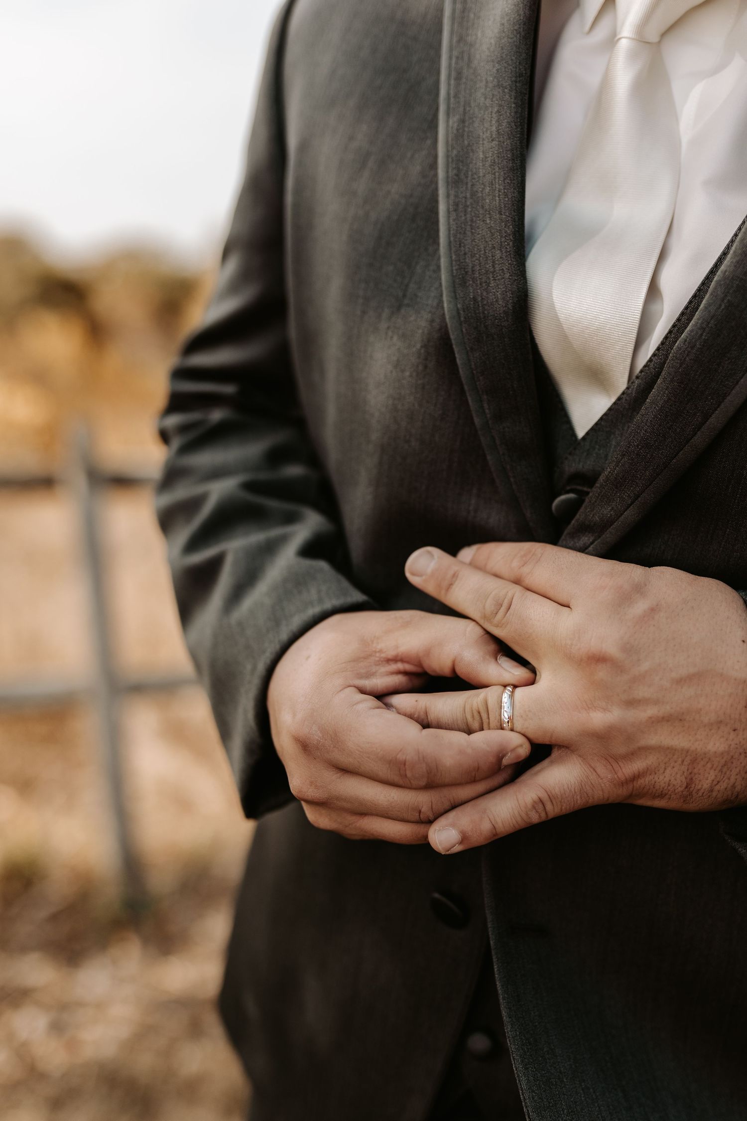 Close-up of hands adjusting wedding ring on finger with black suit jacket.