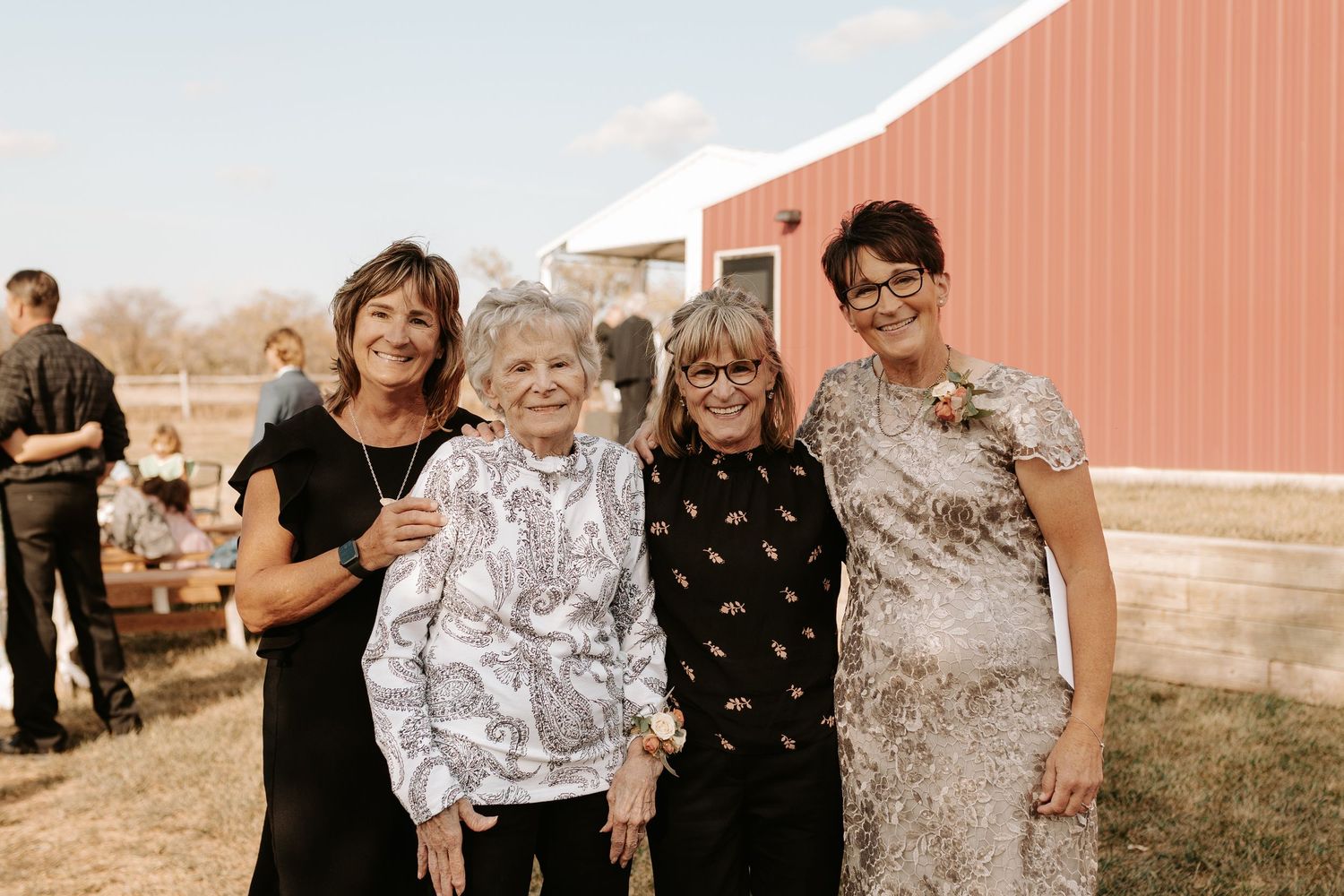 Group gathering outside red barn during countryside wedding celebration.