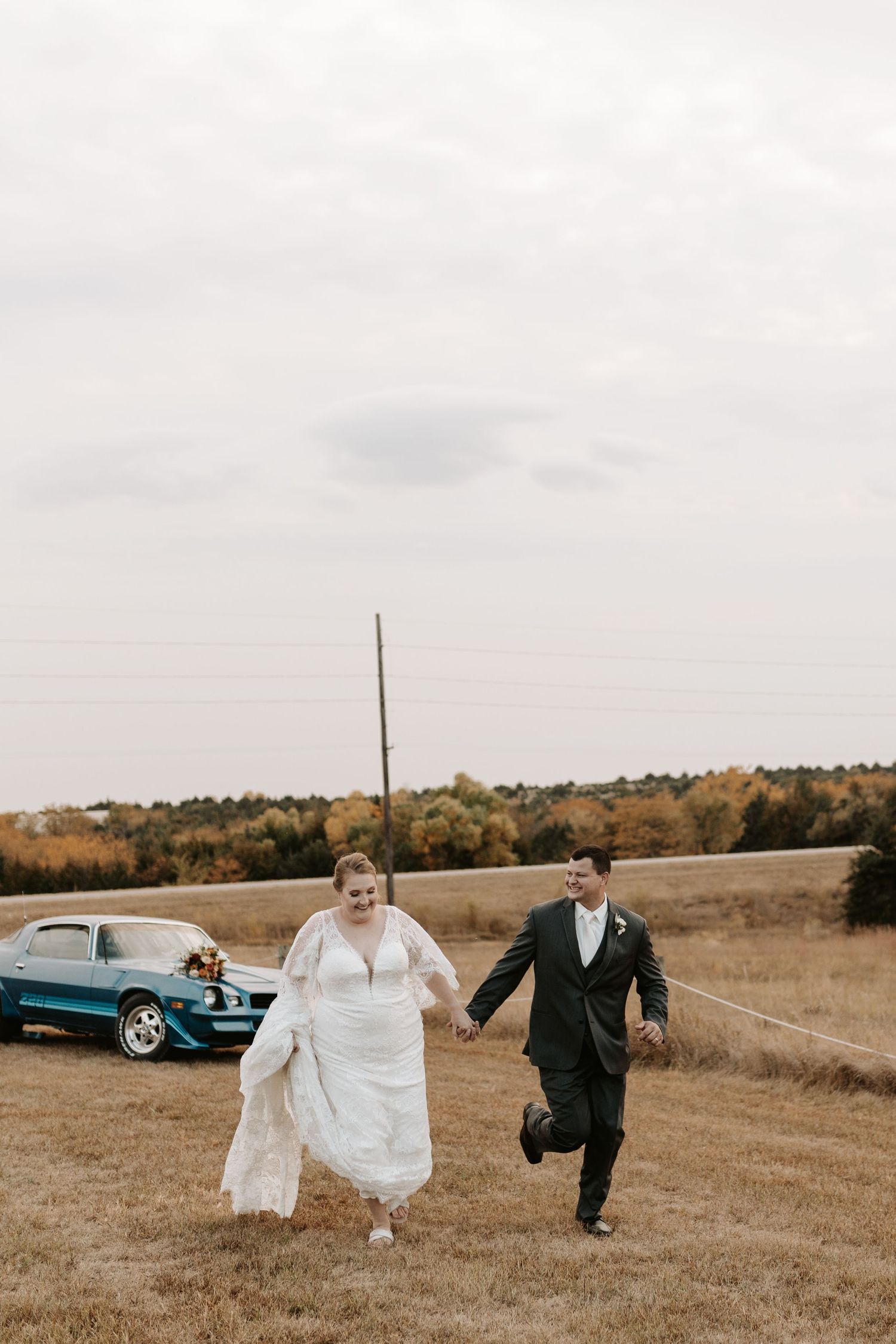 A couple shares a laugh while walking through an autumn field during their wedding photoshoot.
