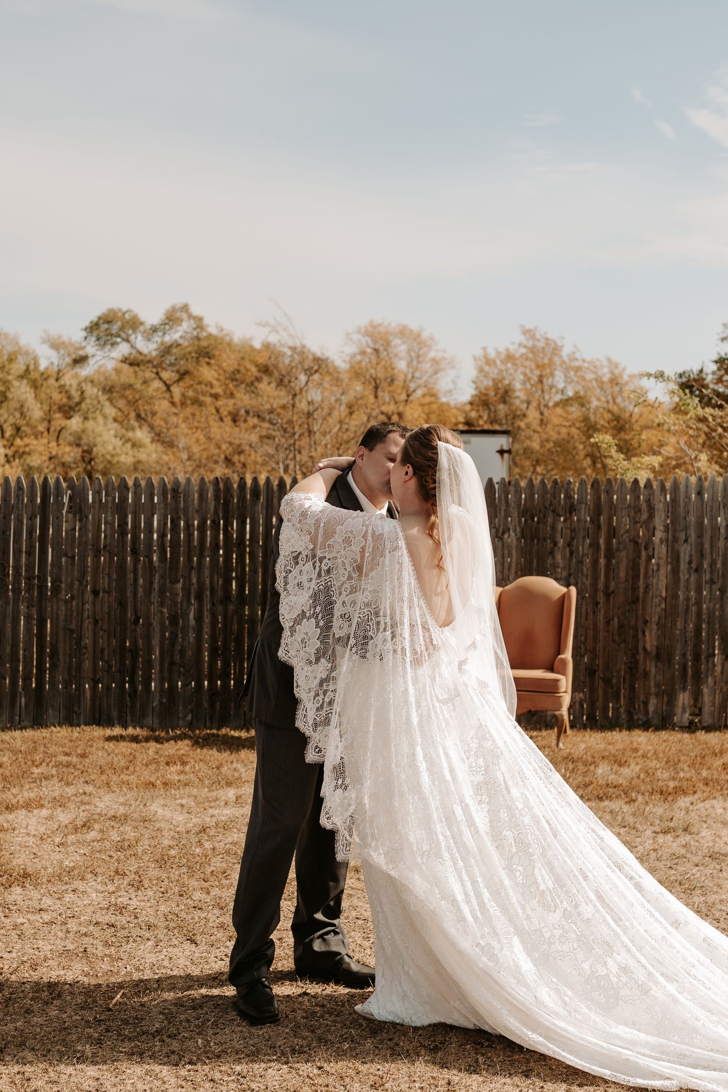 Romantic outdoor wedding moment with vintage chair and wooden fence backdrop.