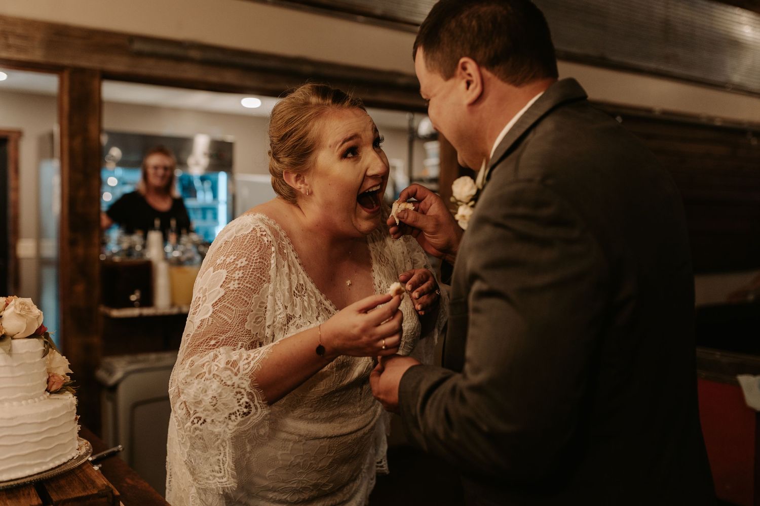 Couple sharing a joyful moment while sharing cake at their wedding reception.