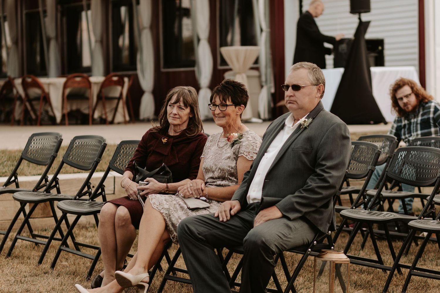 Wedding guests seated on folding chairs at outdoor venue.