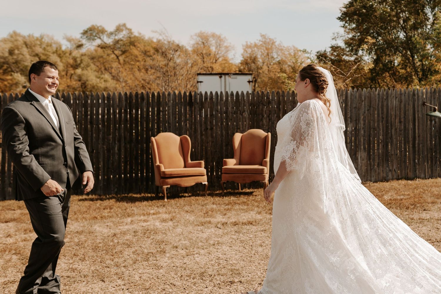 Outdoor wedding scene with vintage chairs and wooden fence in autumn setting.