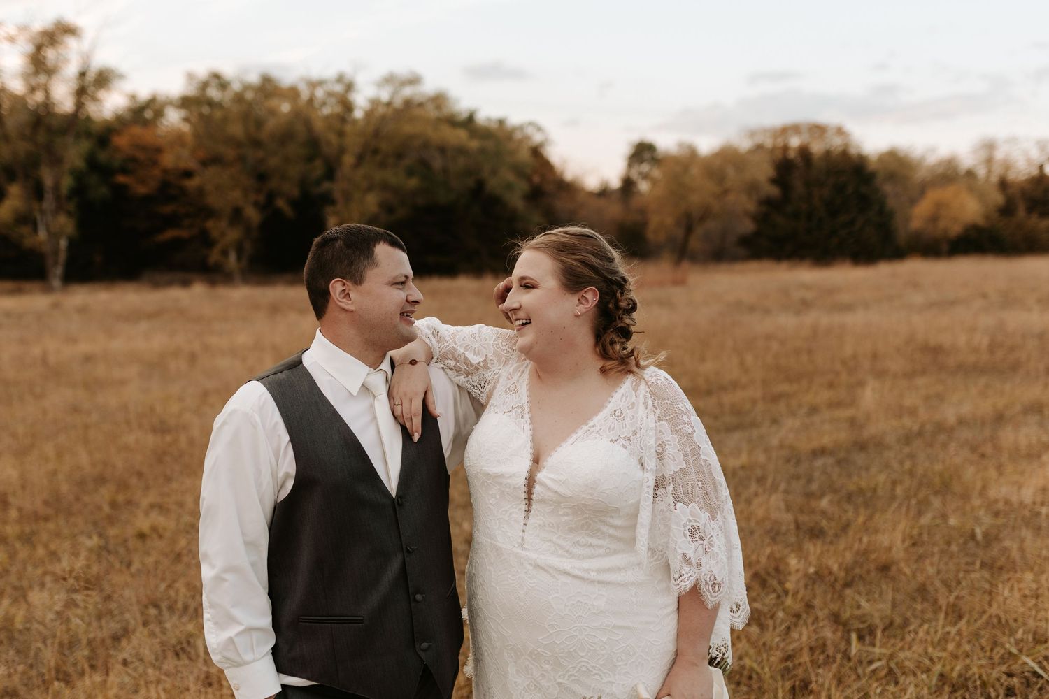 Newlyweds share a candid laugh together in front of autumn trees.