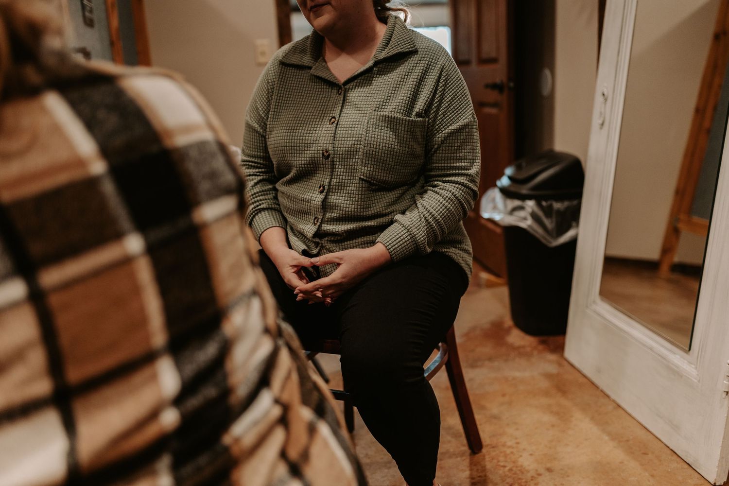 Person in olive green shirt sitting on chair during wedding preparations.