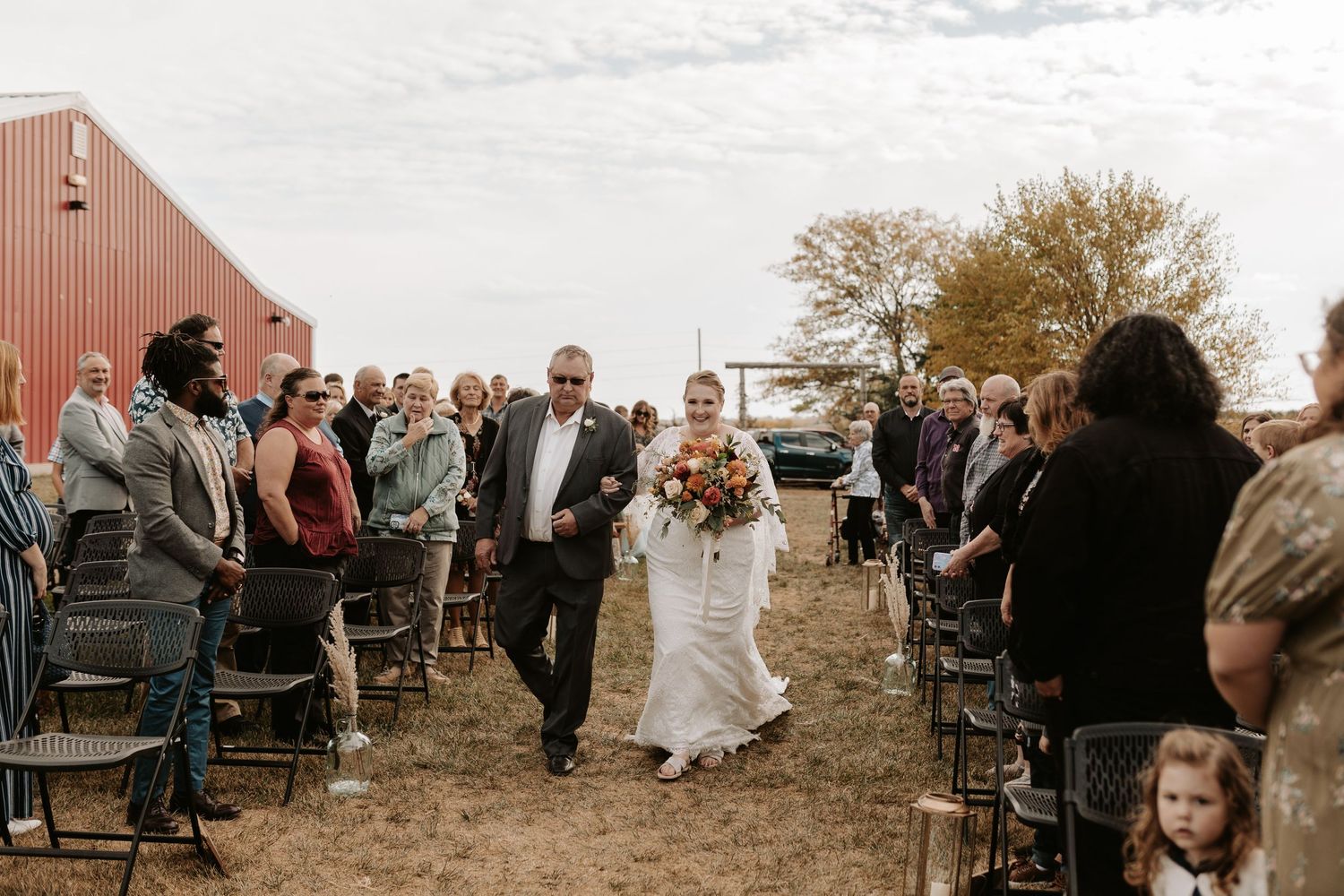 Outdoor barn wedding ceremony with guests lining the aisle during processional.