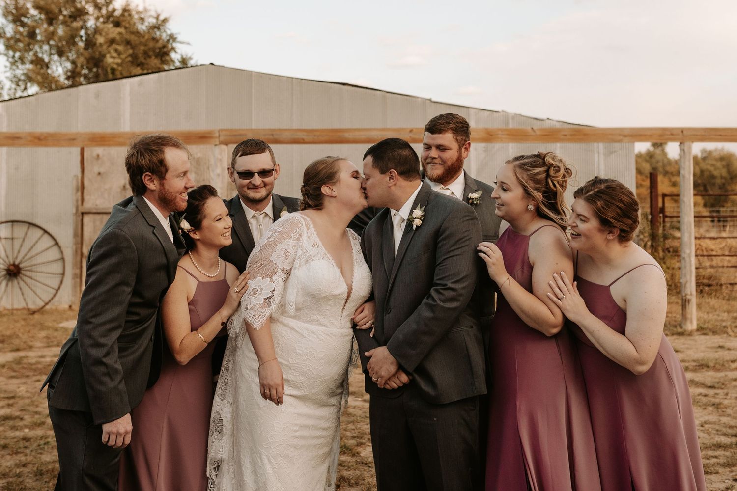 A joyful wedding party in mauve dresses and dark suits sharing laughter during golden hour.