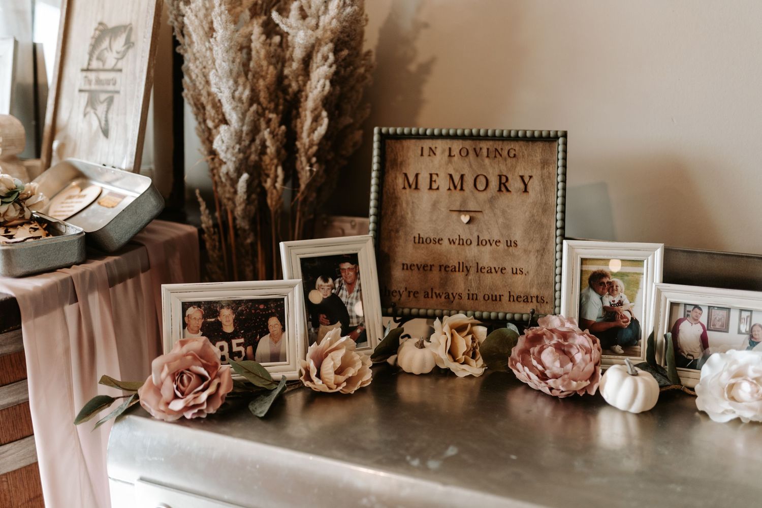 Memorial display with vintage photos, roses, and 'In Loving Memory' sign on table.