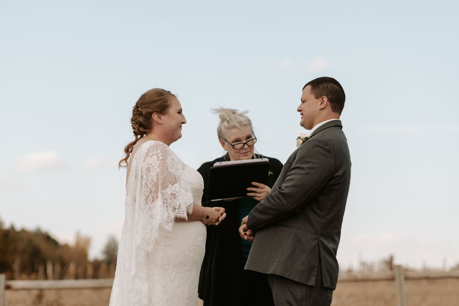 An outdoor winter wedding ceremony takes place with an officiant and couple against a natural landscape background.