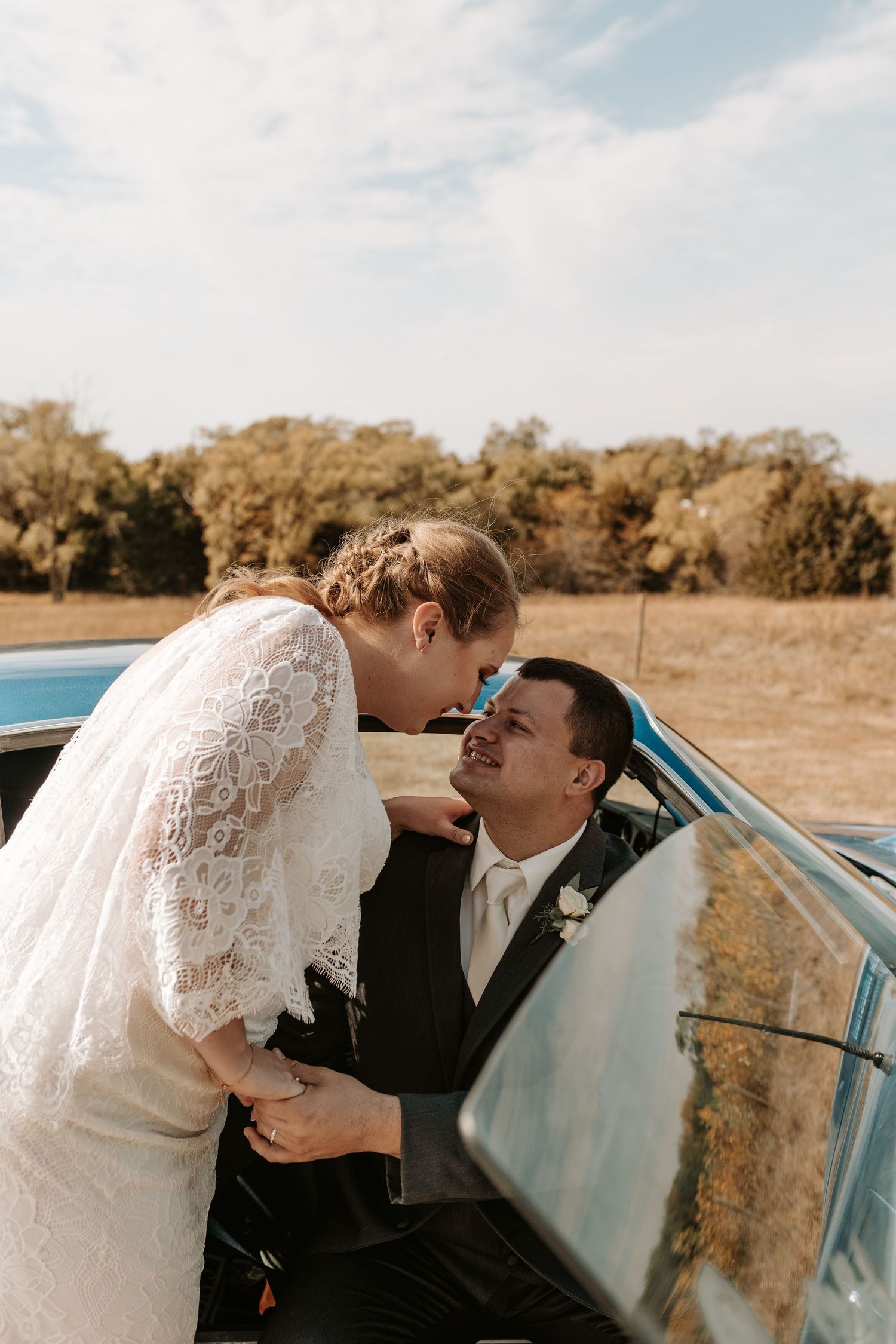 Romantic moment between newlyweds in vintage car during autumn wedding.