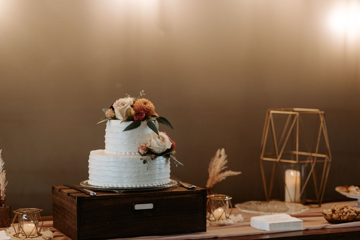 Elegant white wedding cake with floral decoration displayed on wooden box with geometric decor.